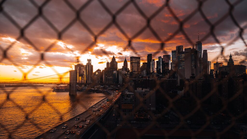 Cityscape skyline at sunset seen through a fence.